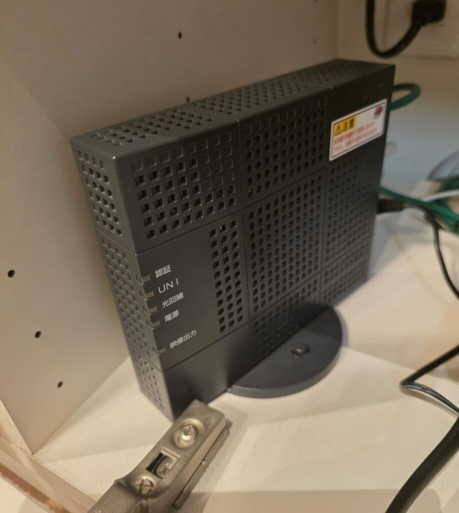 パソコン本体の設定や、バッファロー製の無線ルーター、配線周りを詳しく確認していく中で、原因の根幹が見えてきました。 インターネットの信号を外から引き込んでいる一番根元にある【NTTの黒い通信機器（ONU）】のランプを確認したところ、通電しているはずの電源ランプが完全に消灯して沈黙していたのです。コンセントの電気はしっかりきているため、これはNTTの機器本体が寿命などによって内部で完全に故障してしまっている状態でした。ネットとテレビが同時に全滅した原因はここにあります。