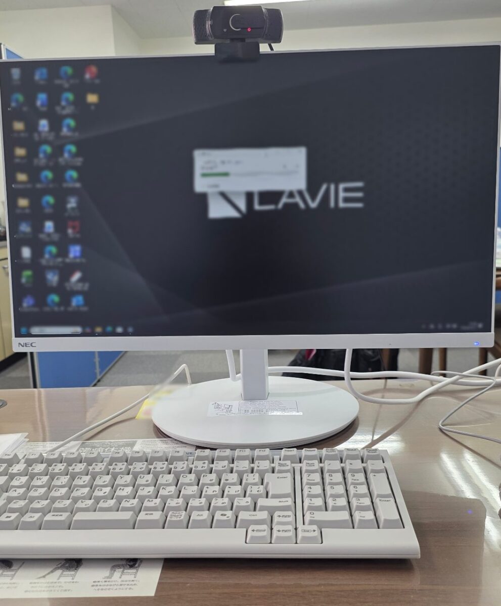 NEC製モニターと白いキーボードが設置されたデスク。モニターにはNEC LAVIEのロゴとWindowsの起動画面らしき表示がある。